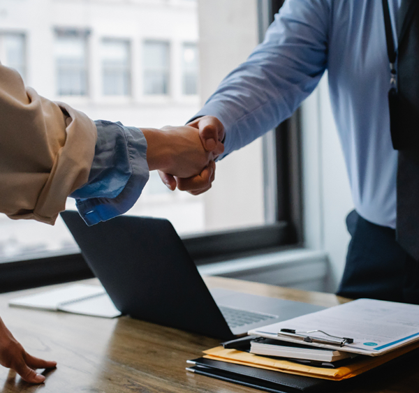 Two people shake hands over a laptop. A rusted resource in knowing what a DICOM PACS migration is.