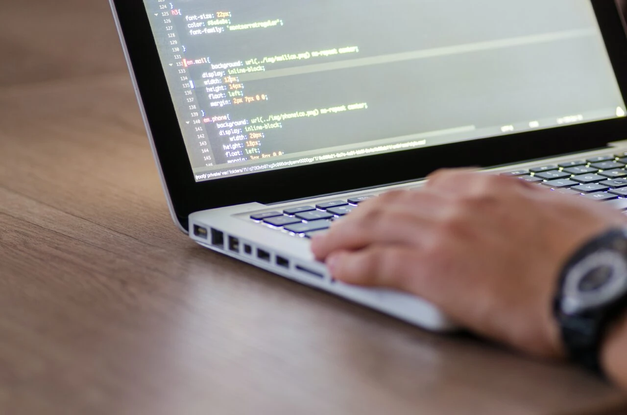 A hand rests on the keyboard of a laptop. Its screen is covered in code as the user works their way through a PACS DICOM migration